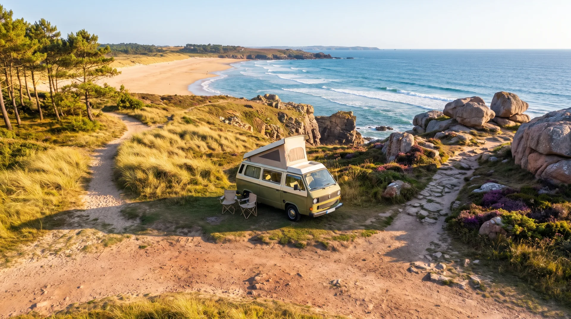 Een groen-wit camperbusje met hefdak staat op een rotsachtige klif met uitzicht op een strand en de zee.